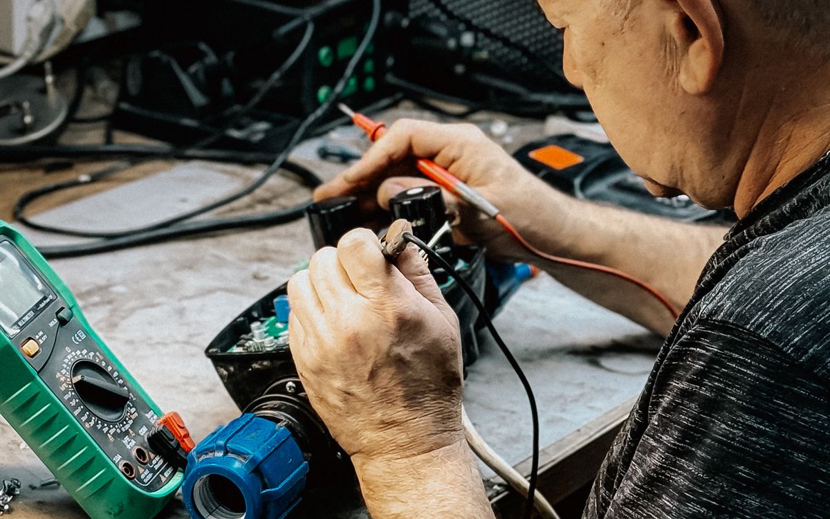 Technician repairing electronics with a soldering iron and multimeter